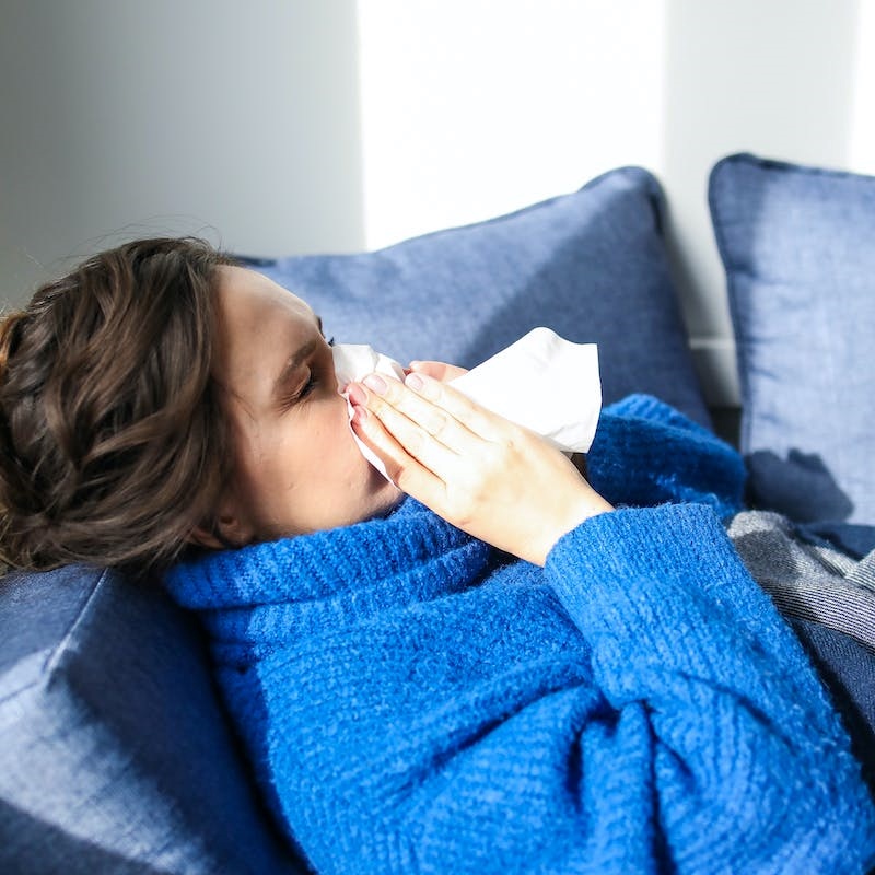 a woman with cold blowing her nose on a tissue paper