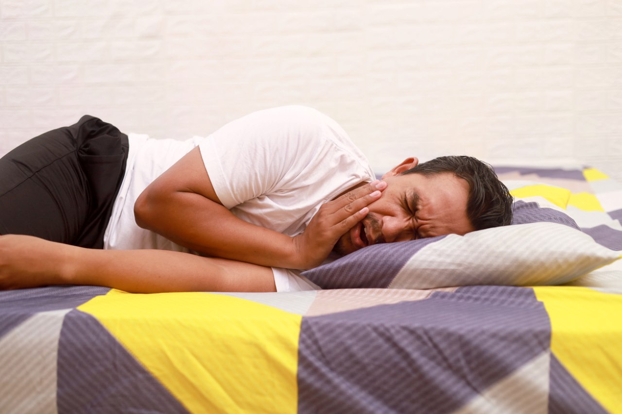 man lying in bed with severe toothache