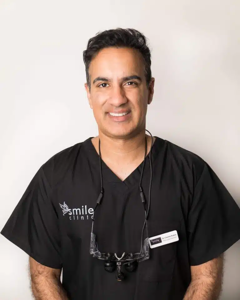 smiling dentist dr. chetan kaher, wearing black scrubs and dental loupes.