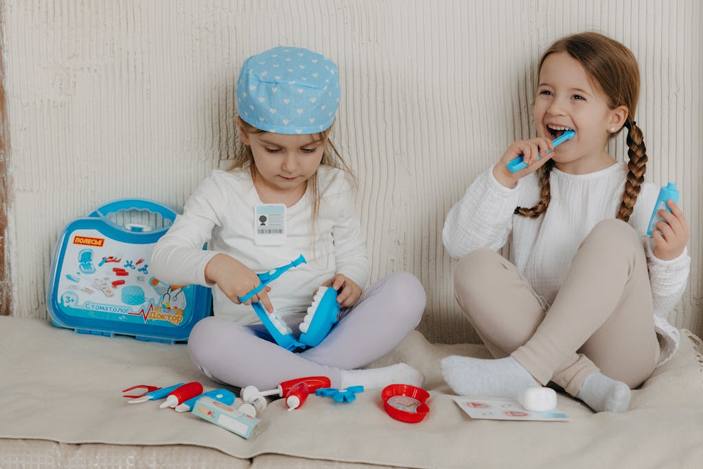Two Young Girls Having Fun Playing Dentist With A Toy Kit Indoors, Enjoying Imaginative Play. two young girls having fun playing dentist with a toy kit indoors, enjoying imaginative play.